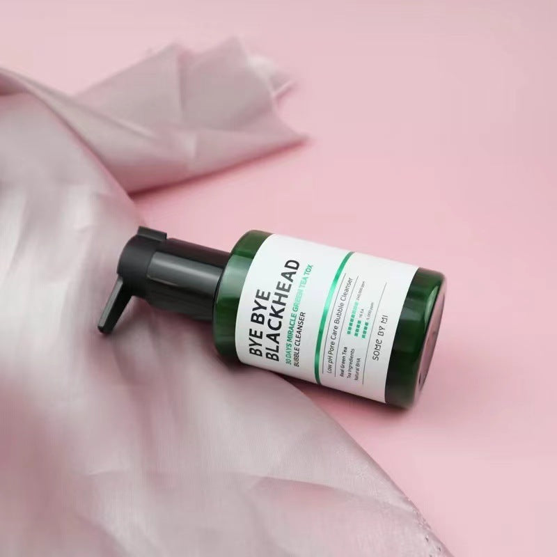 Bye Bye Blackhead green tea facial cleanser in green pump bottle on pink fabric background